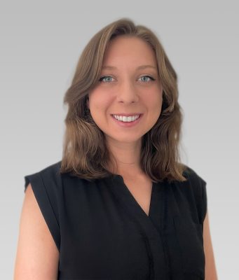 Mackenzie Carney indoor headshot in black shirt against grey background