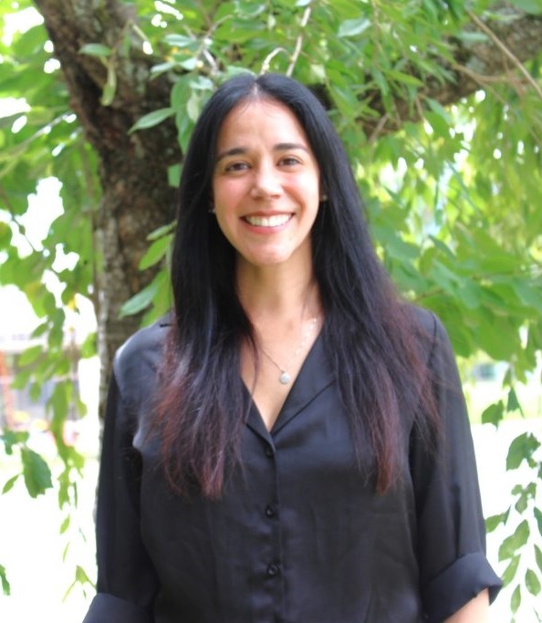 Outdoor headshot of student Isabel Valdivia wearing black standing in front of greenery